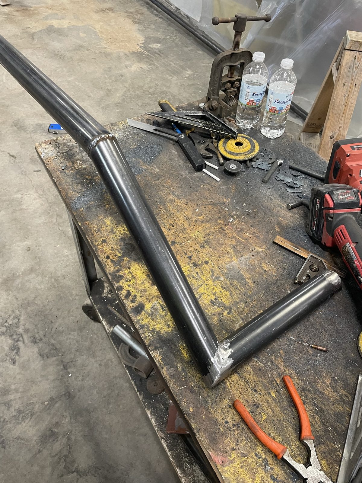 Steel tubing being welded into a custom motorcycle frame piece, tools scattered on the work bench